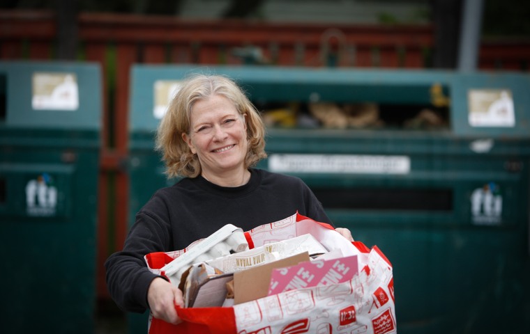 Kvinna står på en återvinningsstation med en kasse pappersförpackningar i famnen